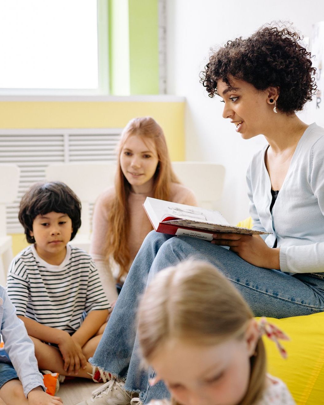 A teacher reads aloud to a small group of children gathered around her
